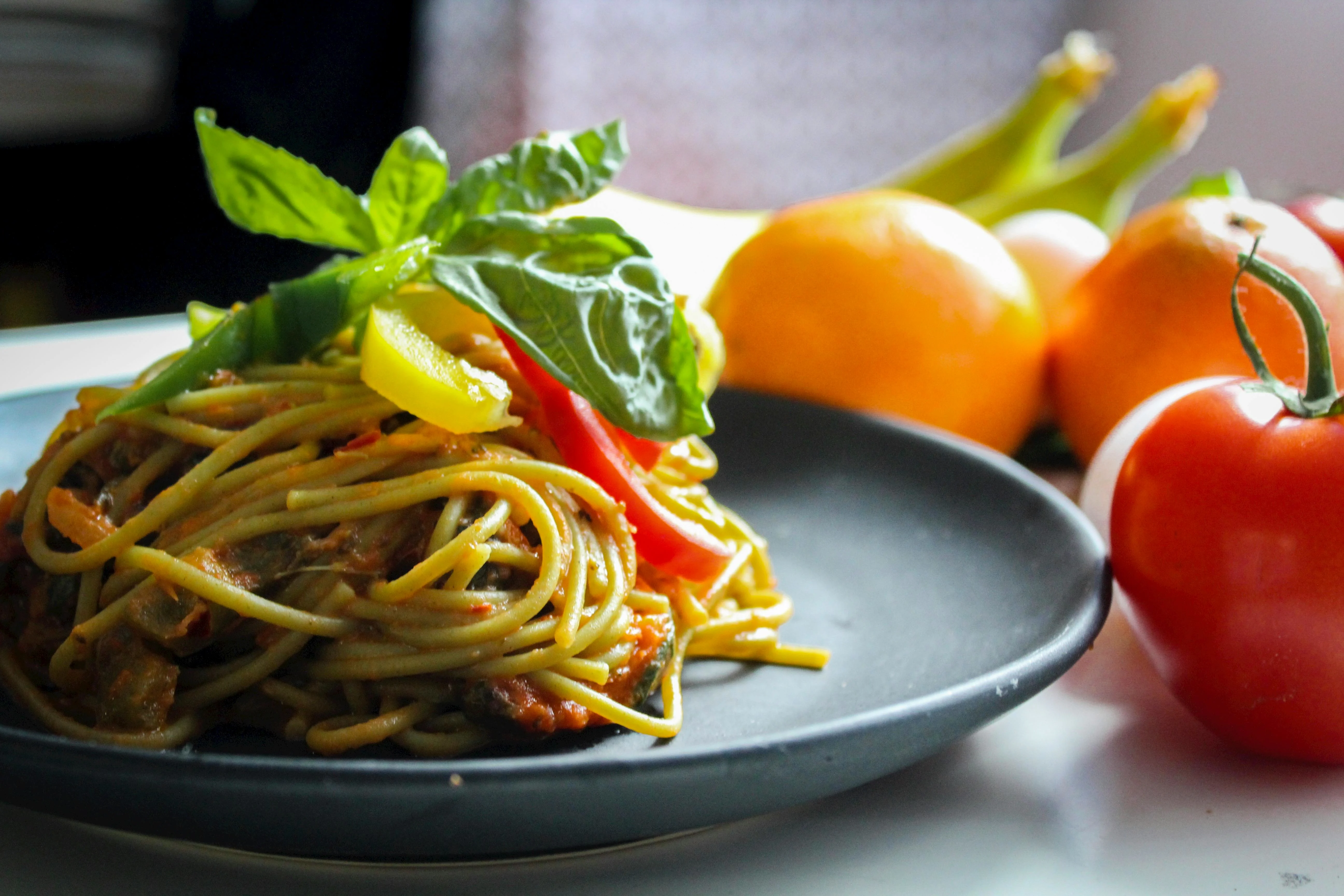 Free Pasta With Vegetable Dish on Gray Plate Beside Tomato Fruit on White Table Stock Photo